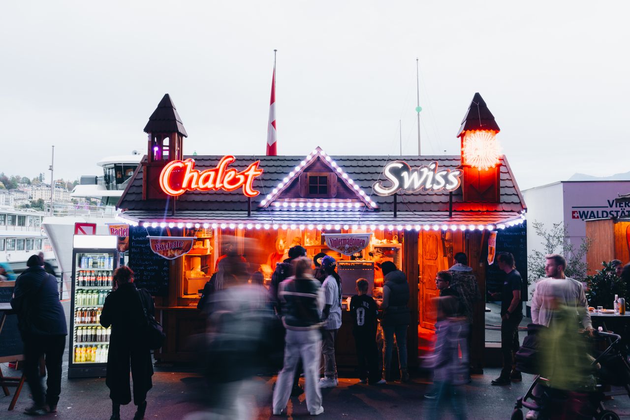 services-03 A vibrant Swiss chalet street food stand with people mingling in an evening festive atmosphere.
