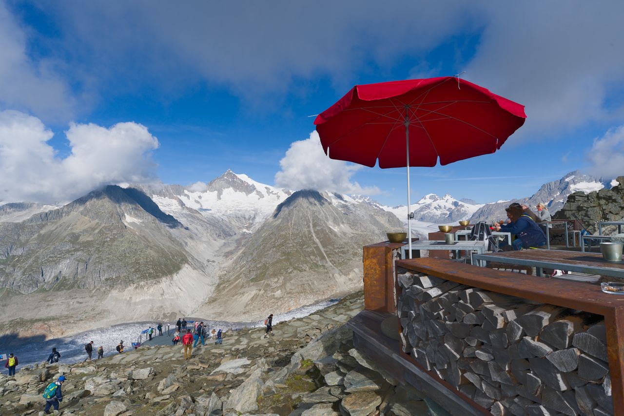 gallery-6 Enjoy a breathtaking view of the Swiss Alps from a mountainside cafe with a vibrant red umbrella.