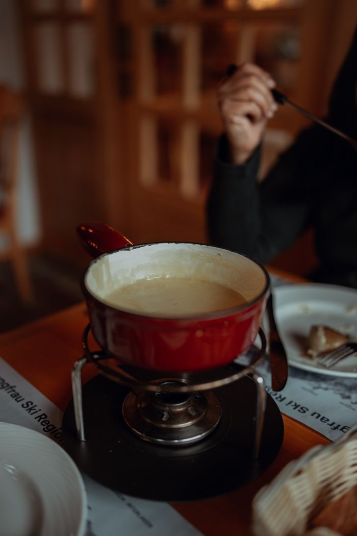 services-02 Warm and inviting cheese fondue in a red pot with dipping bread at a cozy restaurant.