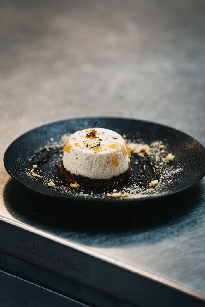 about-02 Elegant cheesecake garnished with honey and nuts served on a modern black dish in a stylish kitchen setting.
